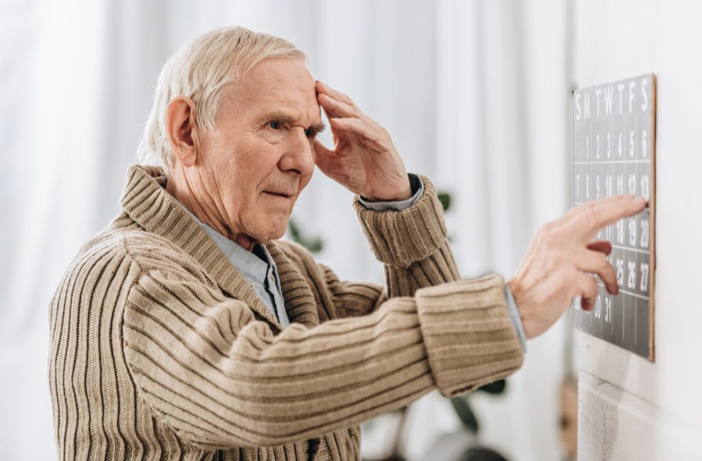 Senior man with dementia looking at wall calendar and touching his head confused.