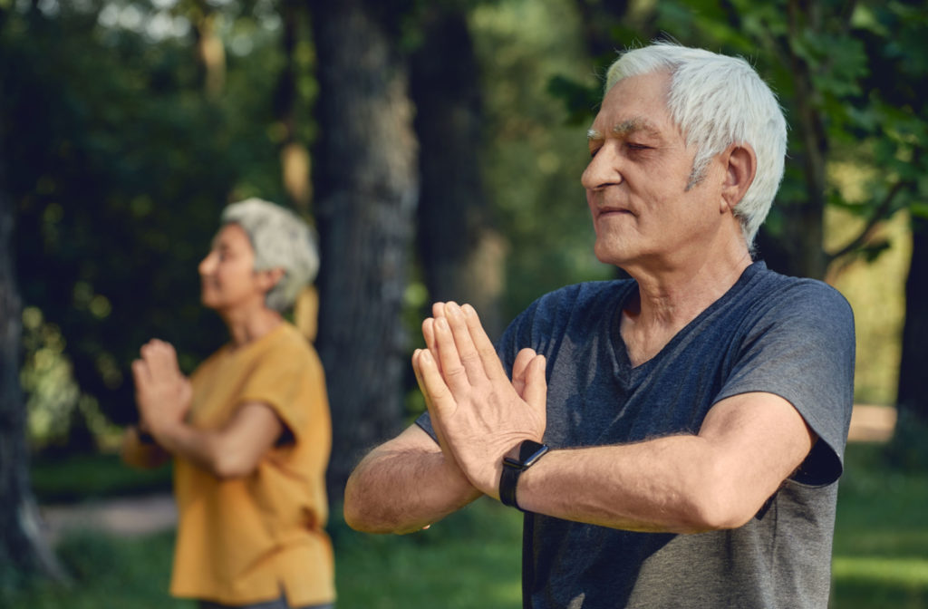 An older adult man and an older adult woman with closed eyes doing yoga in a park.