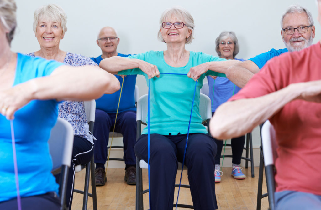 A group of older adults smiling sitting and exercising with resistance bands.