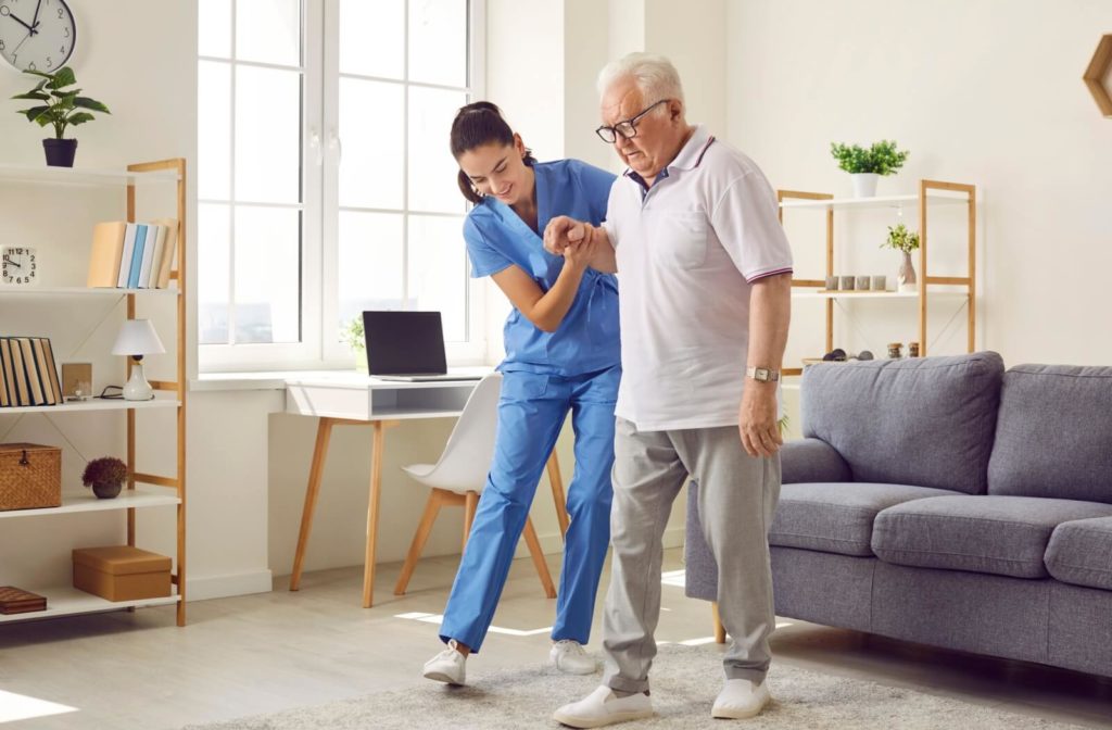 A smiling nurse helping a senior man walk through his apartment in respite care.