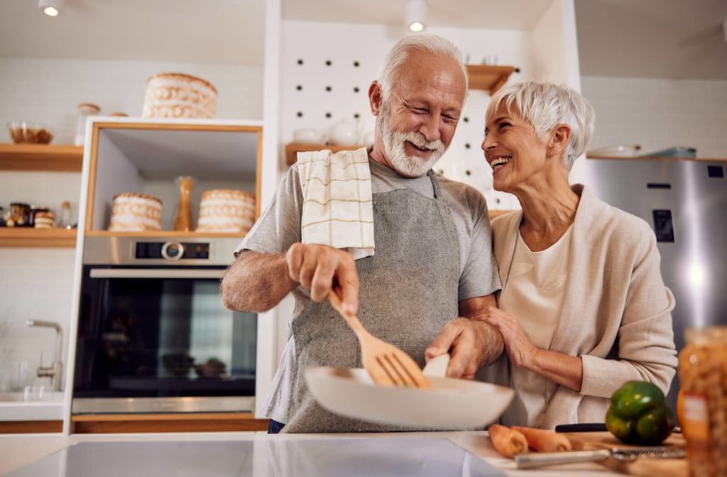 A senior couple smiling in their kitchen while preparing dinner, trying a new recipe to boost their appetite.
