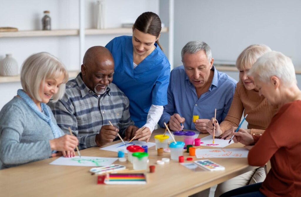 A group of seniors enjoy a painting class provided by their assisted living home with the assistance of a caregiver