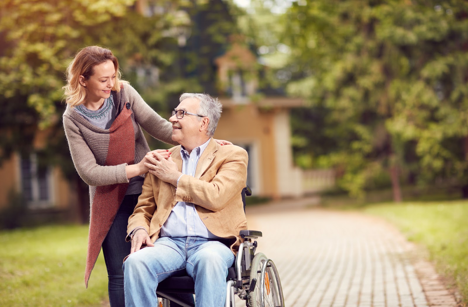 Senior in wheelchair with her daughter as they walk through the park.