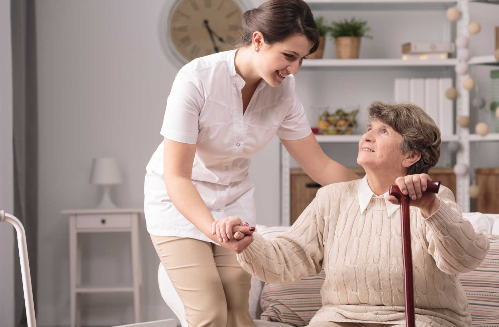 A young carer assisting a senior woman with Alzheimer's by holding her hand and providing support as they walk together.