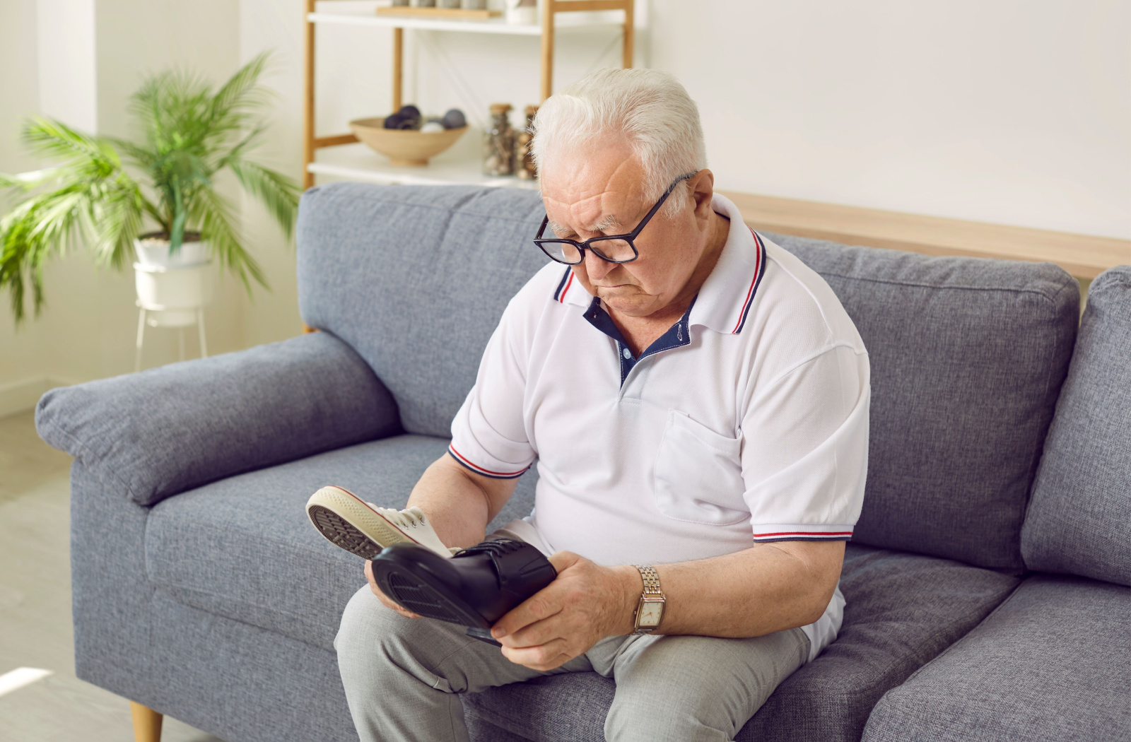 A senior man sitting on a sofa choosing between classic and modern shoes.