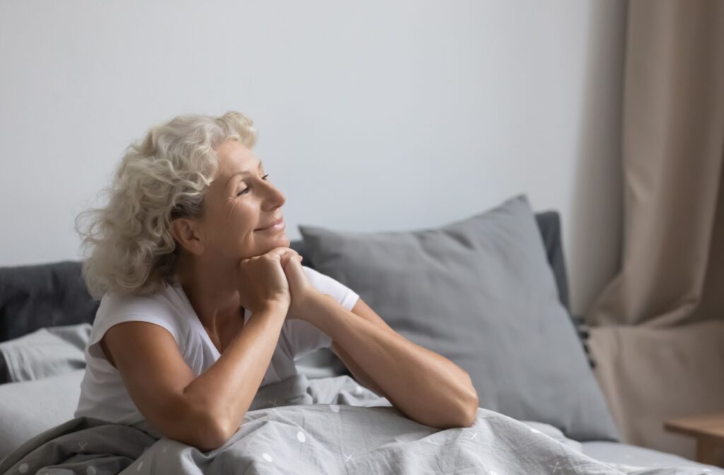Older adult sitting up in bed looking refreshed and well-rested in a bright, cozy bedroom.