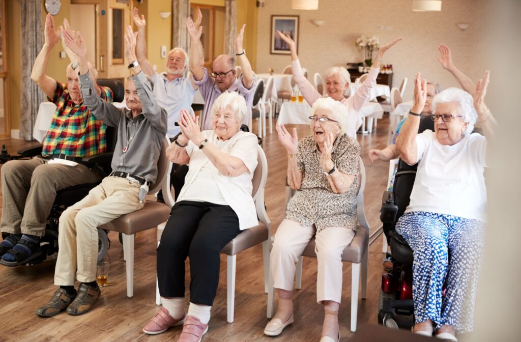 A group of older adults in senior living stretching their arms overhead during a chair yoga class.