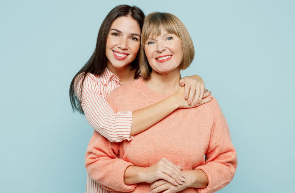 A young adult hugging their older friend in front of a blue background.