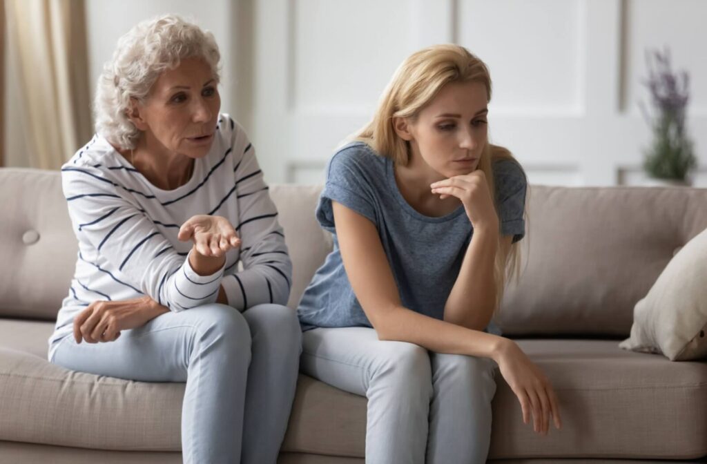 Older adult and younger adult sitting on a couch in serious conversation both appearing thoughtful and emotionally tense