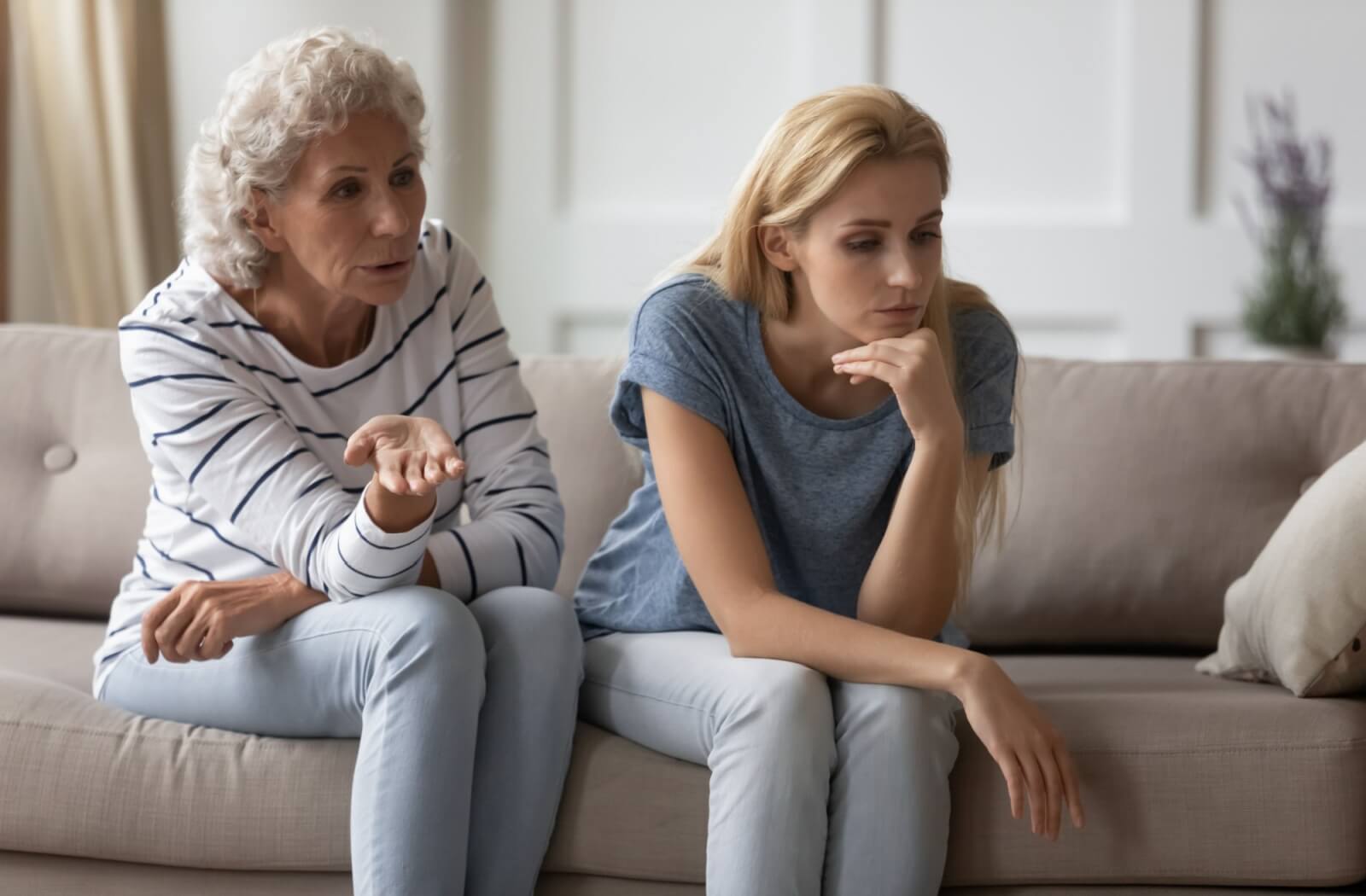 Older adult and younger adult sitting on a couch in serious conversation both appearing thoughtful and emotionally tense