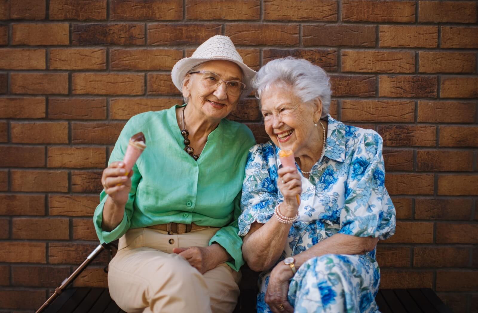 Two older adults enjoying ice cream together on a bench during a summer social event outside