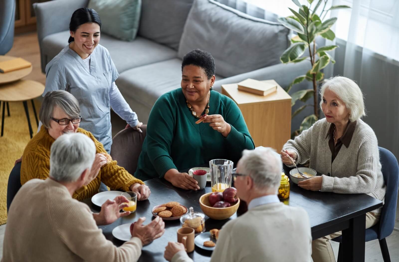 An assisted living caretaker checks in on a group of seniors enjoying a healthy and nutritious breakfast
